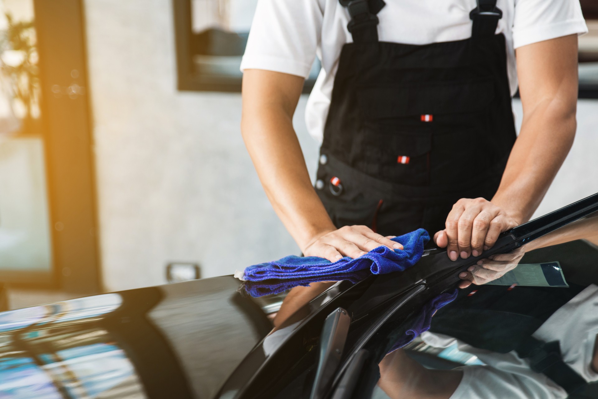 A man cleaning car and remove a scratch with dry blue microfiber towel, car detailing (or valeting) concept. Automobile professional cleaning service. Selective focus.